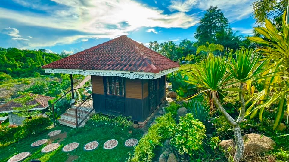 A stilted bahay kubo cottage with a red tile roof among garden plantings